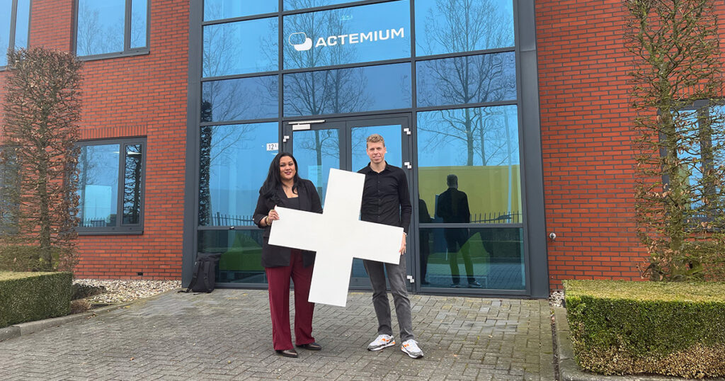 Twee hr-professionals in een kantooromgeving die samen een groot wit plusteken vasthouden.