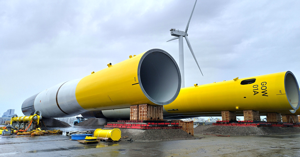 Twee grote cilindervormige windmolentorens liggen op een terminal voor offshore wind in Rotterdamse haven